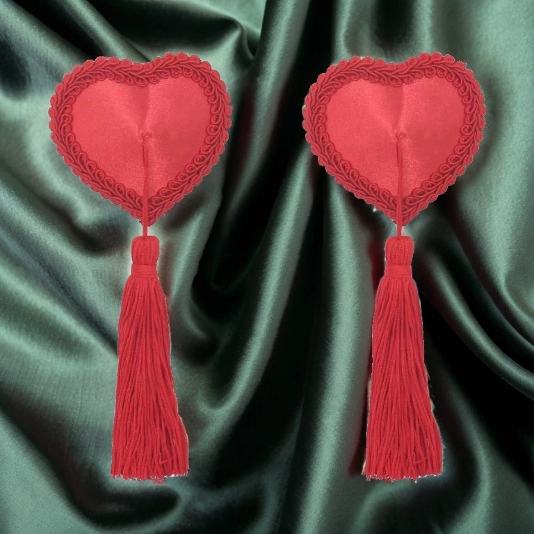 A pair of red heart-shaped nipple pasties with elegant braided trim and playful tassels. These seductive, reusable adhesive covers add a flirty and burlesque-inspired touch to intimate wear, perfect for lingerie styling or performance outfits.